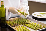 Hands with fresh asparagus and oil in kitchen