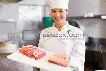 Smiling female chef holding tray of cut meat in kitchen