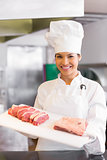Smiling female chef holding tray of cut meat in kitchen