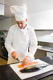 Concentrated male chef cutting fish in kitchen