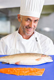 Smiling male chef holding tray of raw fish in kitchen