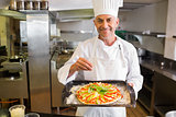 Confident male chef holding cooked food in kitchen