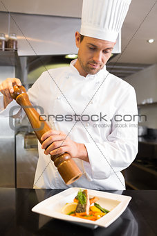 Concentrated male cook grinding pepper on food in kitchen