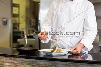 Mid section of a chef garnishing food in kitchen