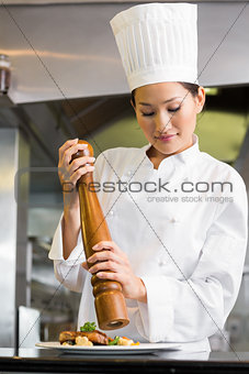 Female cook grinding pepper on food in kitchen