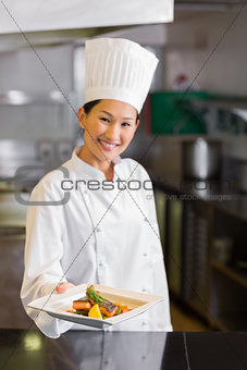 Confident female chef holding cooked food in kitchen