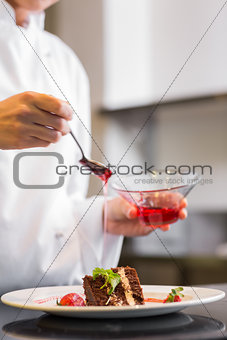 Mid section of a pastry chef decorating dessert in kitchen
