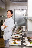 Confident female chef besides cooked food in row at kitchen