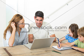 Parents using laptop while children coloring