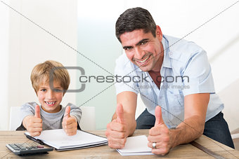 Father and son gesturing thumbs up while doing homework