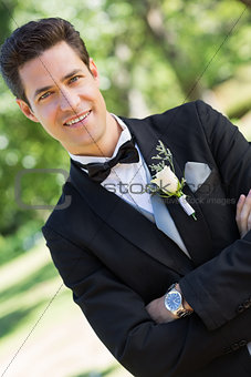 Confident bridegroom with arms crossed in garden