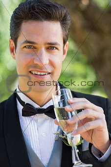 Handsome groom drinking champagne in garden