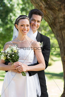 Happy groom embracing bride from behind in garden