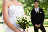 Bride holding bouquet with groom in background