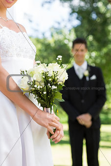 Bride holding bouquet with groom standing in background