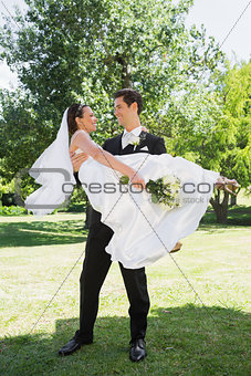 Happy groom carrying bride in arms at garden
