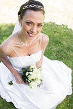 Bride holding flower bouquet while sitting on grass