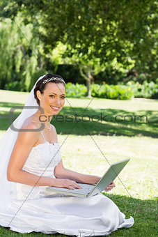 Beautiful bride with laptop sitting on grass
