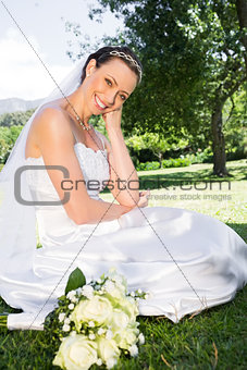 Happy bride sitting on grass in garden