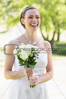 Bride holding bouquet while laughing in garden