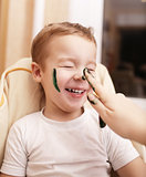 Little boy laughing as his mother paints his face