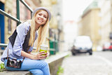 Happy young hipster sitting in the city with cup of hot beverage
