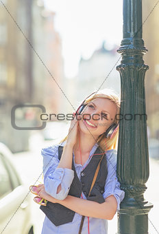 Happy young woman listening music in headphones in the city