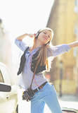 Cheerful young woman listening music in headphones in the city