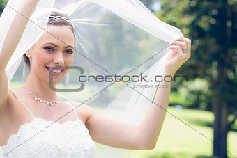 Happy young bride unveiling self in garden