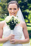 Bride smiling while holding flower bouquet in garden