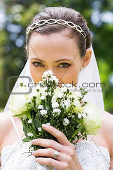 Young bride peeking over bouquet in garden