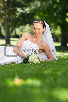 Happy bride lying on grass in park