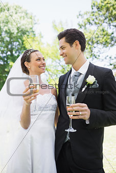 Romantic bride and groom having champagne in park
