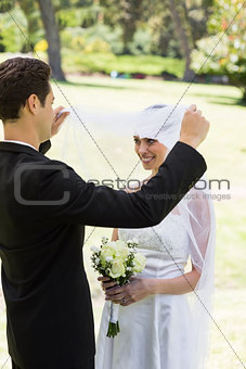 Loving groom lifting veil of bride