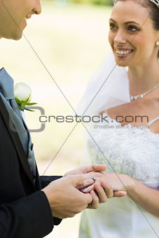Young groom placing ring on brides finger