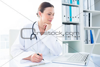 Doctor writing while using laptop