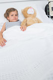Girl with teddy bear lying in hospital bed
