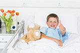 Boy gesturing thumbs up with teddy bear in hospital