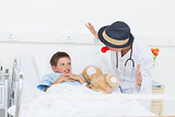 Doctor entertaining sick boy in hospital bed