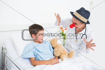 Doctor in clown costume entertaining ill boy in hospital
