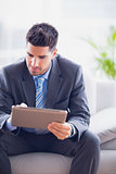 Businessman sitting on sofa using his tablet pc
