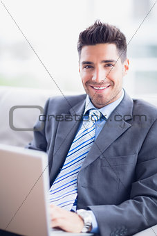 Happy businessman sitting on sofa using his laptop