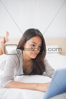 Pretty girl lying on bed using her tablet