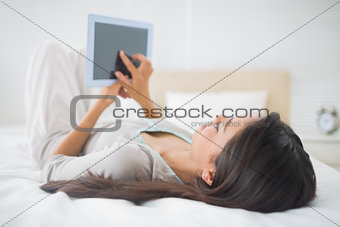 Young girl lying on bed looking at her tablet pc