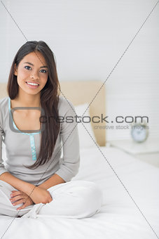 Young pretty girl sitting on bed smiling at camera