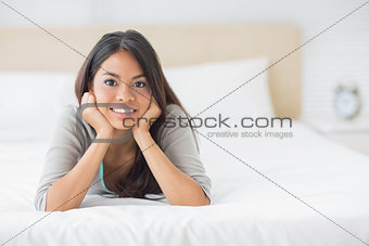 Young pretty girl lying on her bed smiling at camera