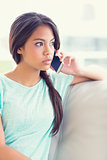Thinking girl sitting on sofa making a phone call