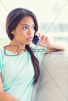 Thinking girl sitting on sofa making a phone call