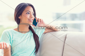 Cheerful girl sitting on sofa making a phone call