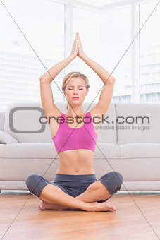 Calm blonde meditating in lotus pose with arms raised